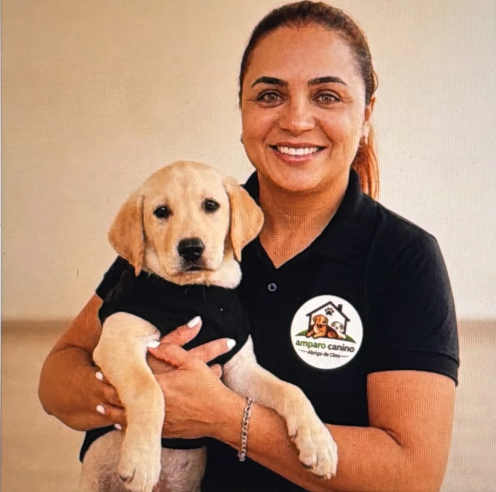 Antonia Mayara sorrindo, segurando um filhote de cachorro no colo, vestindo camisa da Amparo Canino